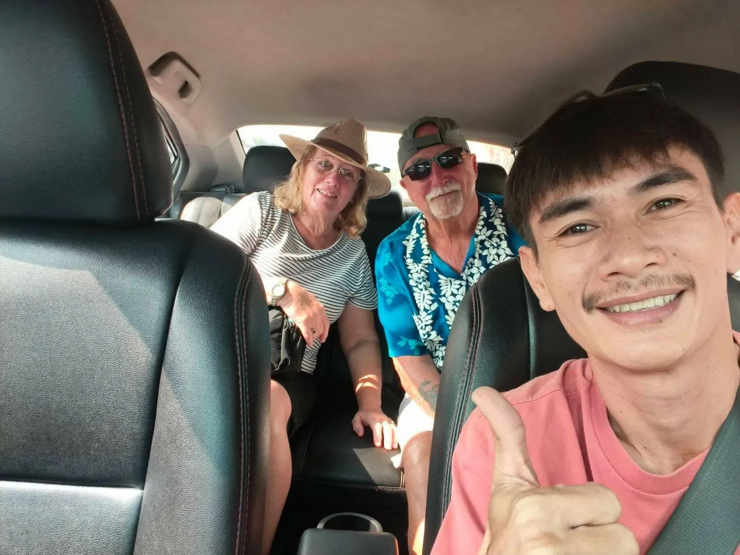 Nong driving a couple, all three giving a thumbs up in the car