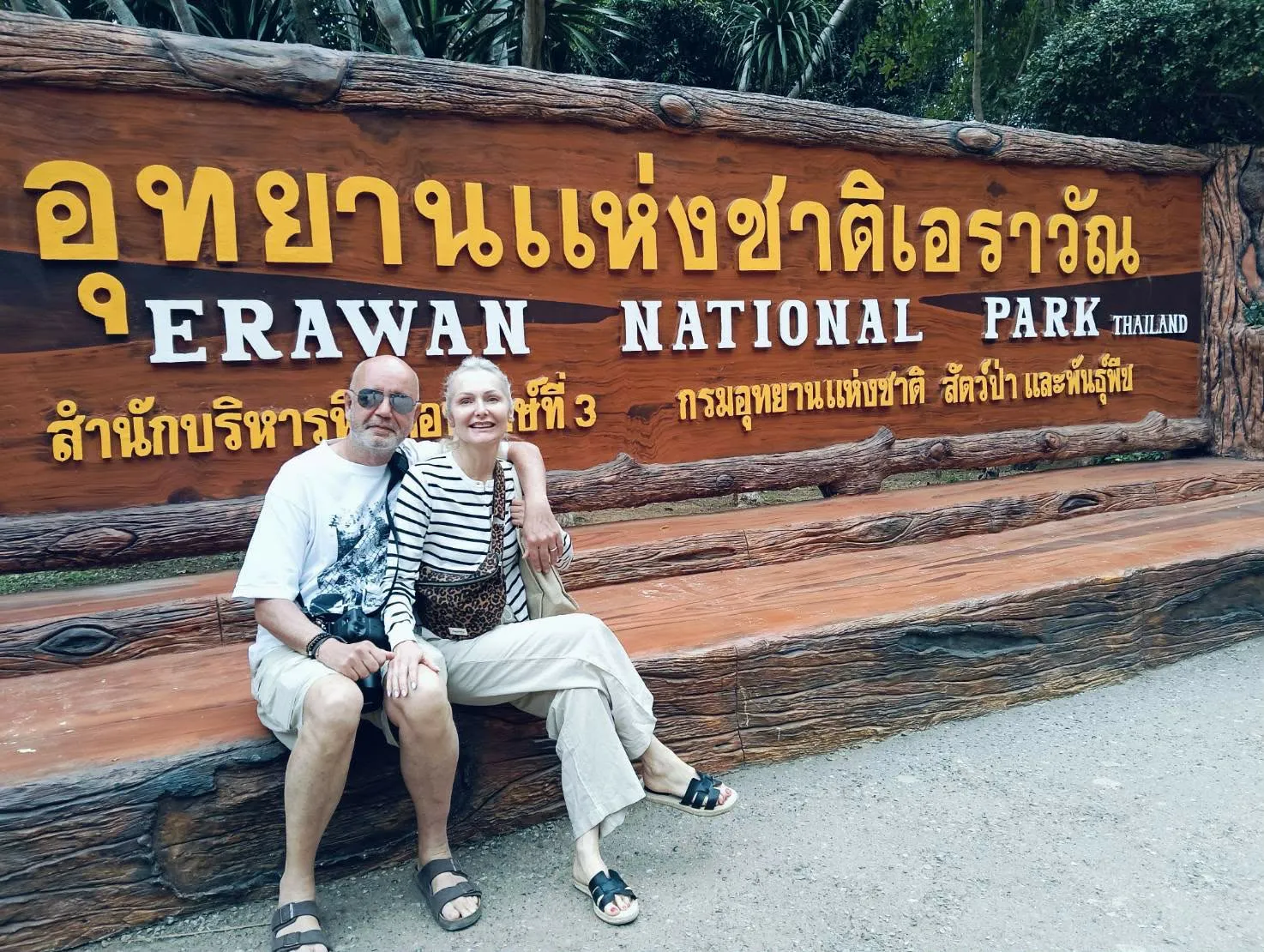 A couple sitting at the Erawan National Park sign
